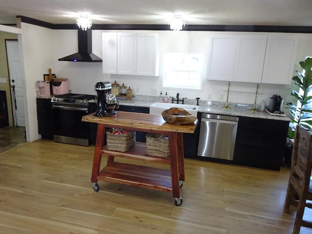 kitchen with light wood finished floors, a sink, white cabinets, appliances with stainless steel finishes, and wall chimney exhaust hood
