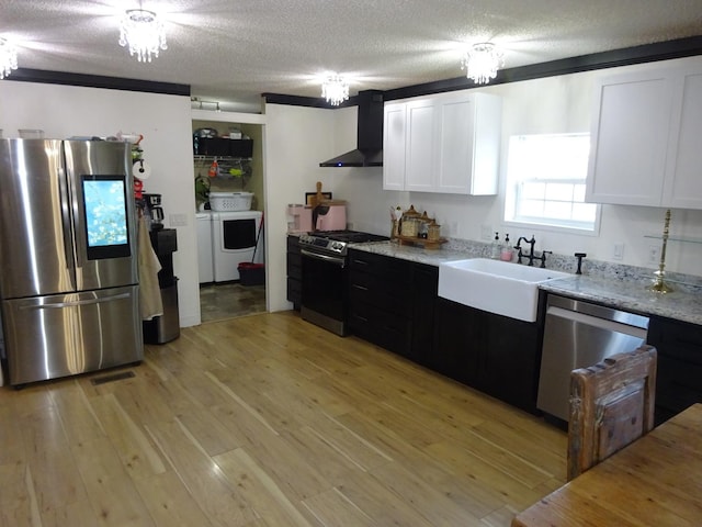 kitchen featuring a sink, white cabinets, appliances with stainless steel finishes, wall chimney range hood, and light wood-type flooring