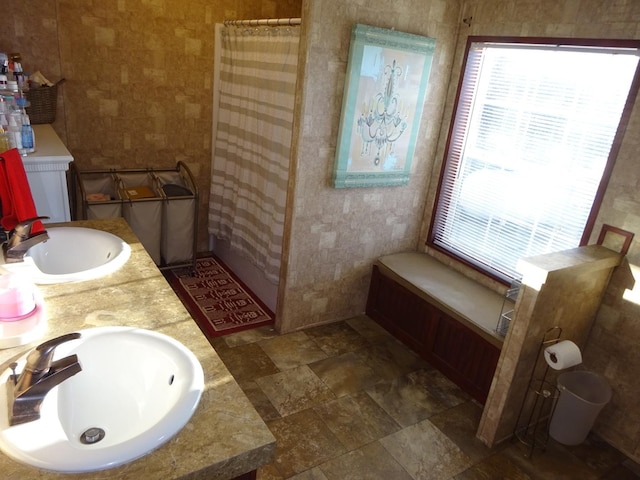 full bath featuring double vanity, stone finish floor, a shower with shower curtain, and a sink