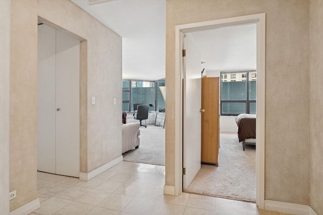 corridor featuring light carpet, light tile patterned floors, and baseboards