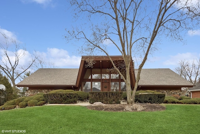 rear view of property featuring stone siding, roof with shingles, and a yard