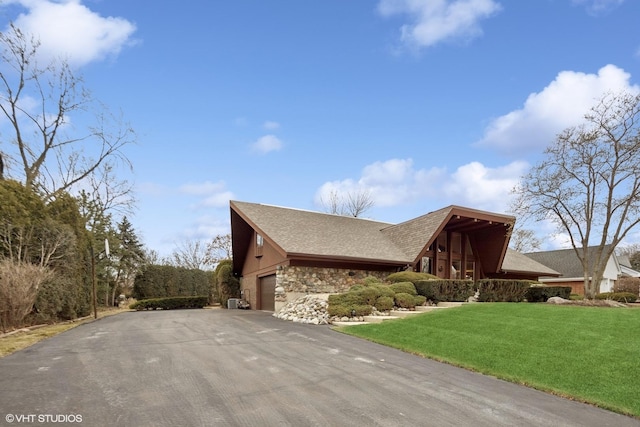 view of property exterior with a garage, a lawn, stone siding, aphalt driveway, and roof with shingles