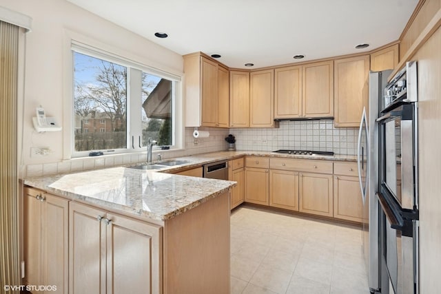 kitchen with light brown cabinets, a sink, appliances with stainless steel finishes, light stone countertops, and tasteful backsplash