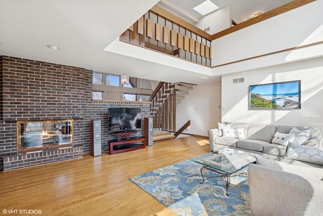 living area featuring visible vents, stairway, a brick fireplace, wood finished floors, and baseboards