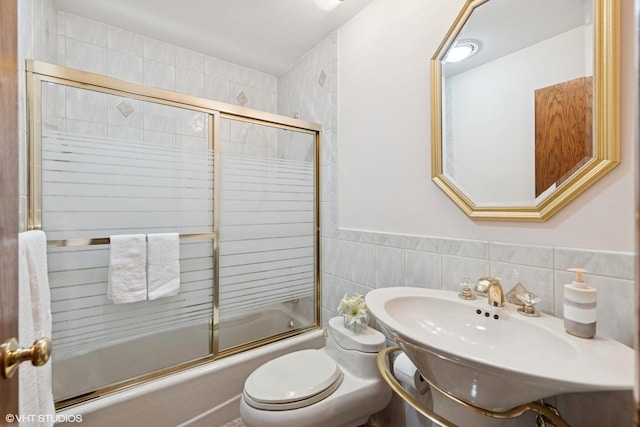 full bath featuring a sink, tile walls, toilet, and bath / shower combo with glass door