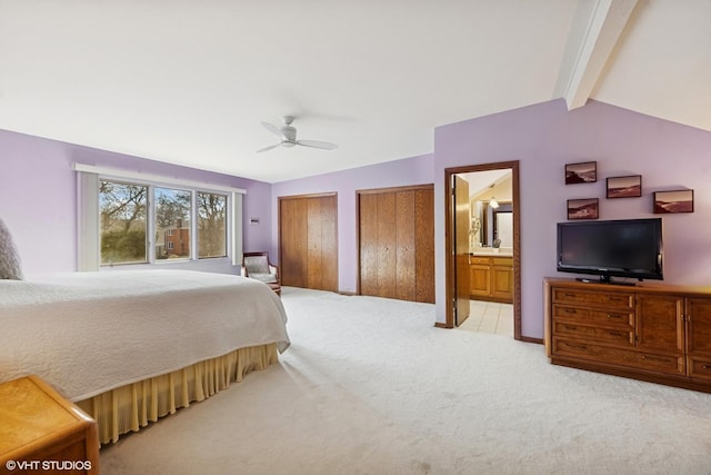 bedroom with vaulted ceiling with beams, connected bathroom, light carpet, a ceiling fan, and multiple closets