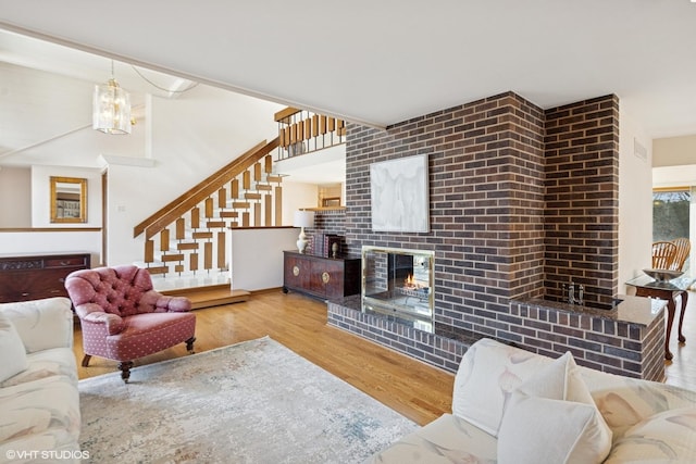 living room featuring stairway, a brick fireplace, wood finished floors, and an inviting chandelier