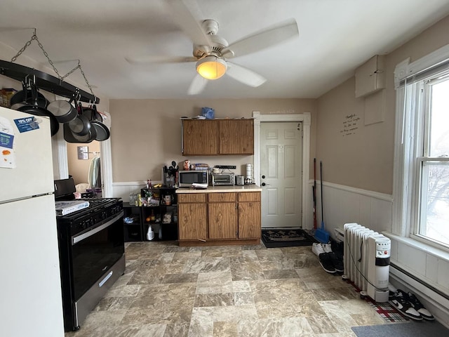 kitchen with stainless steel appliances, light countertops, wainscoting, radiator, and brown cabinetry