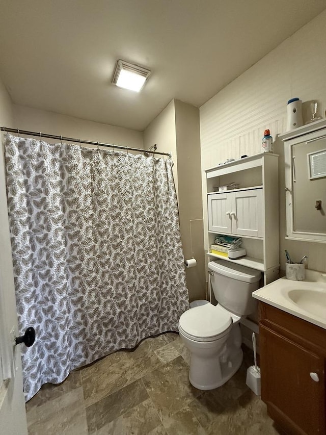 full bath featuring stone finish floor, a shower with shower curtain, vanity, and toilet