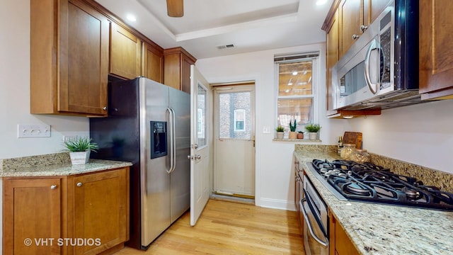 kitchen featuring stainless steel appliances, brown cabinetry, a raised ceiling, and light wood-style flooring