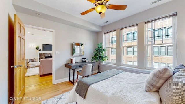 bedroom featuring visible vents, a high end fireplace, light wood-style flooring, and baseboards