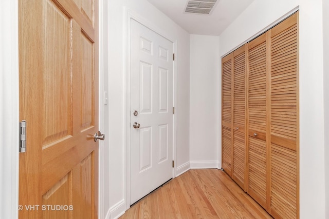 hallway featuring baseboards, visible vents, and light wood finished floors