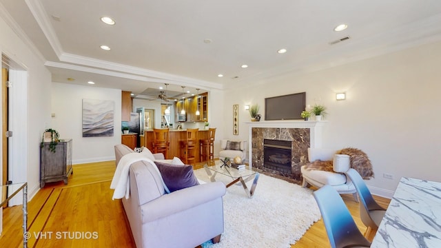 living room featuring crown molding, visible vents, a premium fireplace, light wood-type flooring, and baseboards