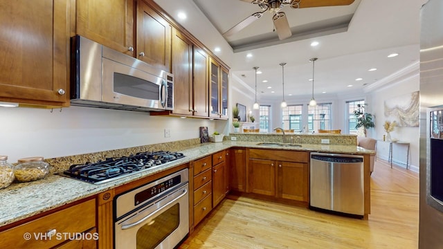 kitchen with appliances with stainless steel finishes, a tray ceiling, brown cabinetry, and a peninsula