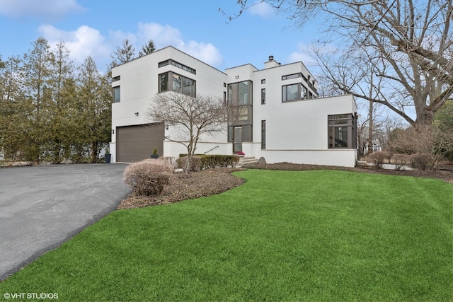 view of front of property with a chimney, aphalt driveway, an attached garage, a front lawn, and stucco siding