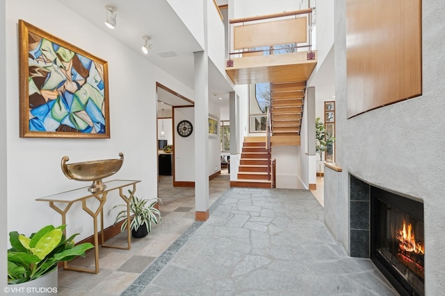 entryway with a towering ceiling, stairway, baseboards, and a glass covered fireplace