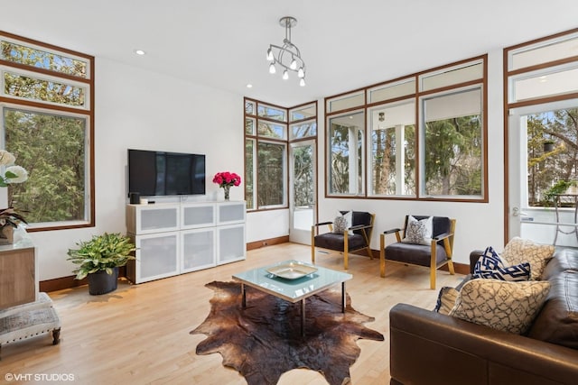 living area with a healthy amount of sunlight, baseboards, a chandelier, and wood finished floors