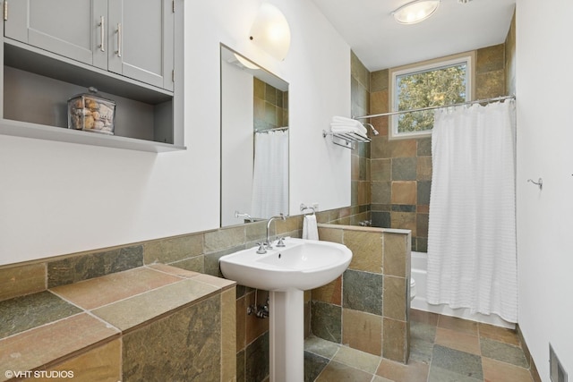 bathroom with stone tile floors, visible vents, shower / bathtub combination with curtain, toilet, and a sink