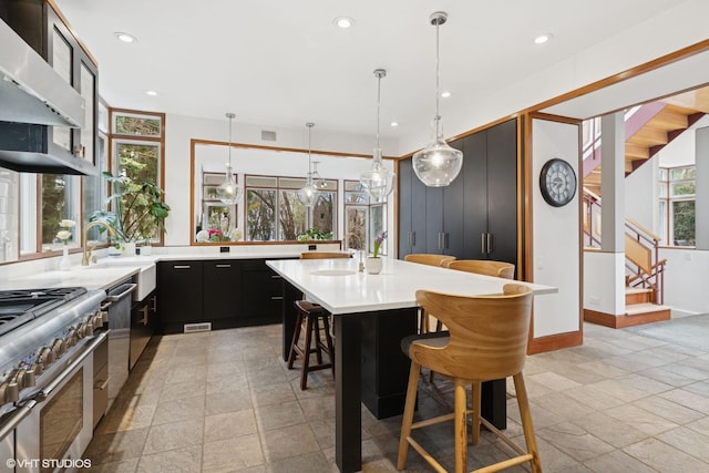 kitchen featuring under cabinet range hood, dark cabinets, a sink, light countertops, and a kitchen bar