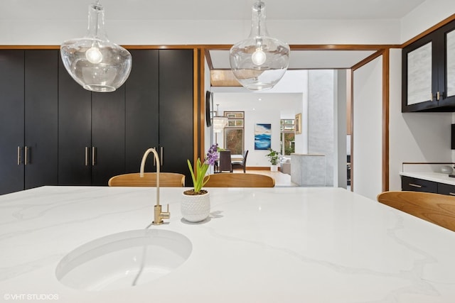 kitchen with light stone counters, pendant lighting, and dark cabinetry