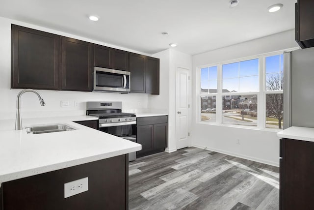 kitchen featuring dark brown cabinetry, wood finished floors, a sink, light countertops, and appliances with stainless steel finishes