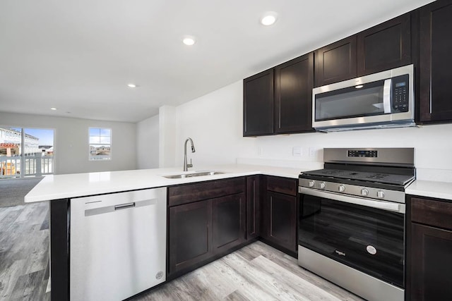 kitchen with stainless steel appliances, a peninsula, a sink, open floor plan, and light countertops