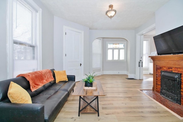 living room with arched walkways, a brick fireplace, light wood-style flooring, and baseboards