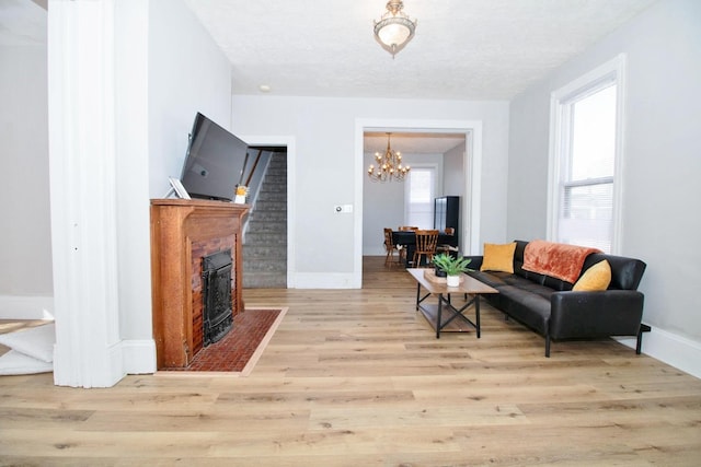 living area with a fireplace with flush hearth, a notable chandelier, wood finished floors, and baseboards