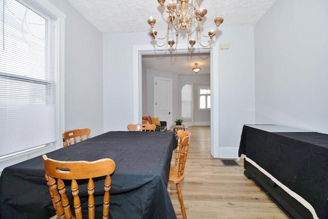 dining room featuring a textured ceiling, light wood finished floors, a chandelier, and baseboards