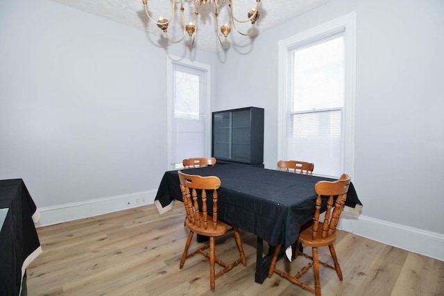 dining space with a chandelier, a textured ceiling, baseboards, and light wood-style floors