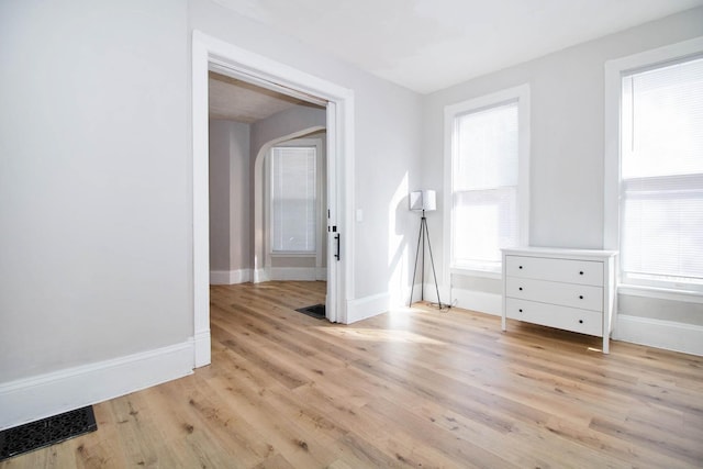 spare room with arched walkways, a healthy amount of sunlight, light wood-style flooring, and baseboards