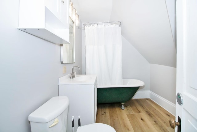 bathroom with toilet, wood finished floors, vaulted ceiling, vanity, and a bath