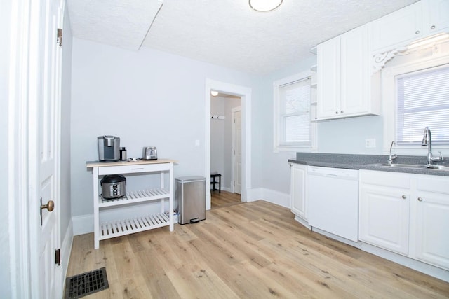 kitchen with a sink, visible vents, white cabinets, light wood-style floors, and dishwasher