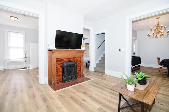 living room featuring wood finished floors, baseboards, stairs, a brick fireplace, and an inviting chandelier