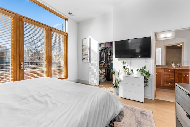 bedroom with a closet, visible vents, light wood-style flooring, ensuite bathroom, and baseboards