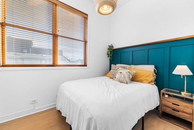 bedroom featuring light wood-style floors, a wainscoted wall, and a decorative wall