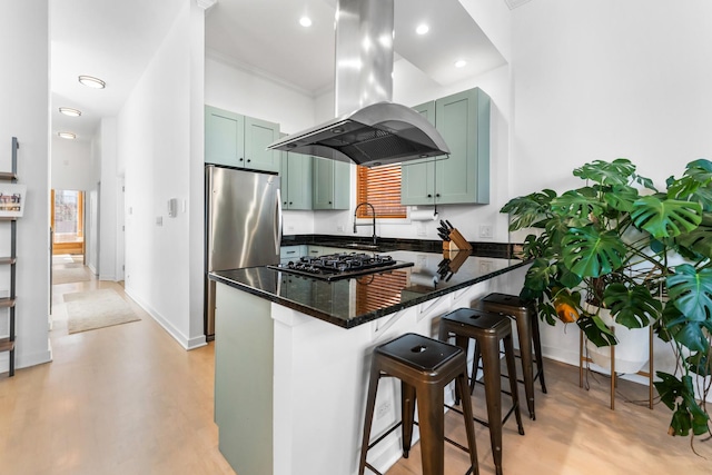 kitchen with a breakfast bar area, stainless steel appliances, a peninsula, dark stone countertops, and island exhaust hood