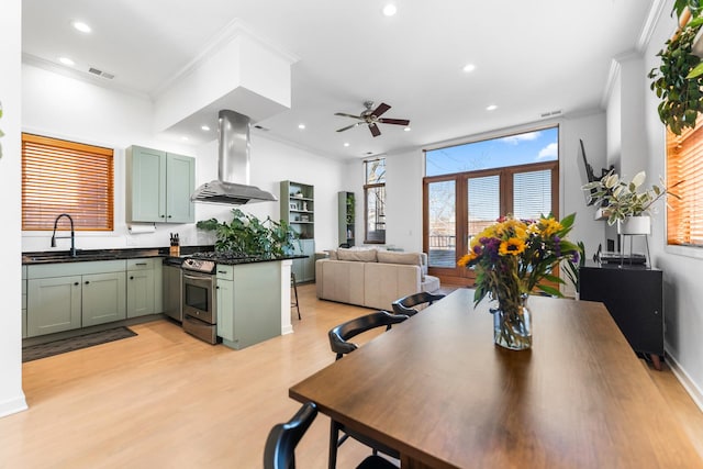 kitchen featuring dark countertops, a sink, stainless steel gas range, ventilation hood, and green cabinetry