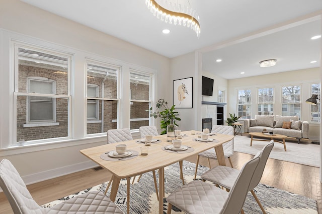 dining space featuring a tiled fireplace, baseboards, wood finished floors, and recessed lighting