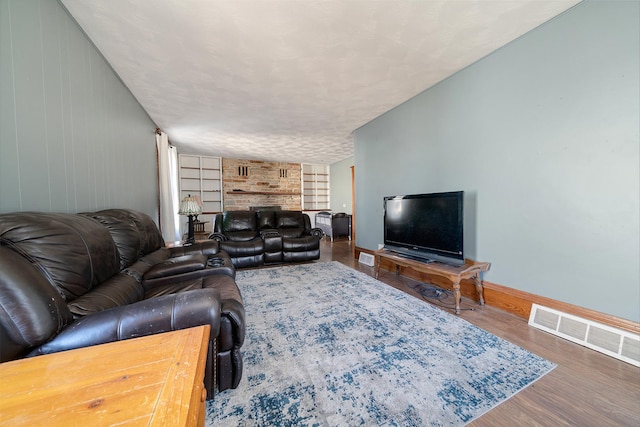 living room with visible vents, baseboards, built in features, wood finished floors, and a textured ceiling