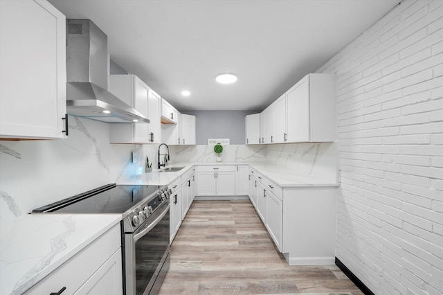 kitchen featuring light stone counters, light wood-style flooring, a sink, stainless steel electric range oven, and wall chimney exhaust hood