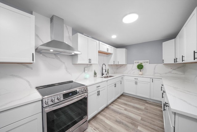 kitchen with a sink, wall chimney range hood, light wood-type flooring, stainless steel electric stove, and tasteful backsplash