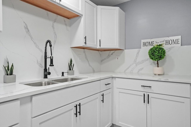 kitchen with backsplash, white cabinetry, a sink, white dishwasher, and light stone countertops