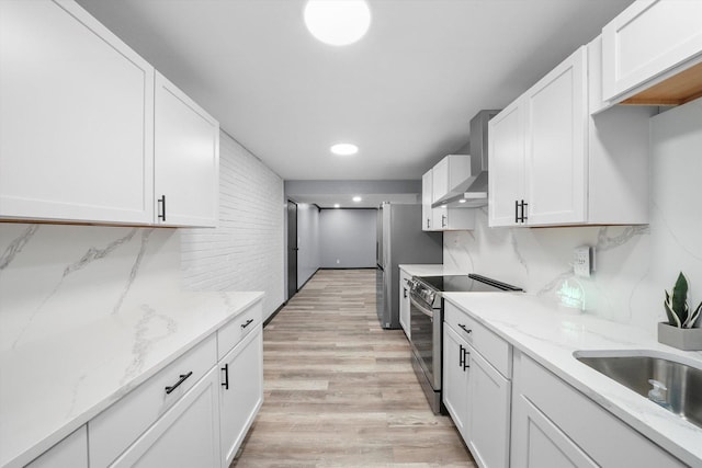 kitchen featuring tasteful backsplash, white cabinets, wall chimney exhaust hood, stainless steel range with electric cooktop, and a sink