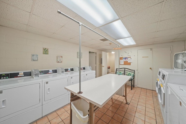 shared laundry area featuring concrete block wall, light tile patterned floors, and independent washer and dryer