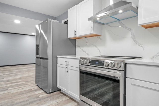 kitchen featuring stainless steel appliances, white cabinetry, light wood-style floors, decorative backsplash, and wall chimney exhaust hood