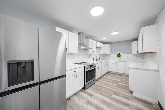 kitchen with white cabinets, decorative backsplash, light wood-style flooring, appliances with stainless steel finishes, and wall chimney range hood