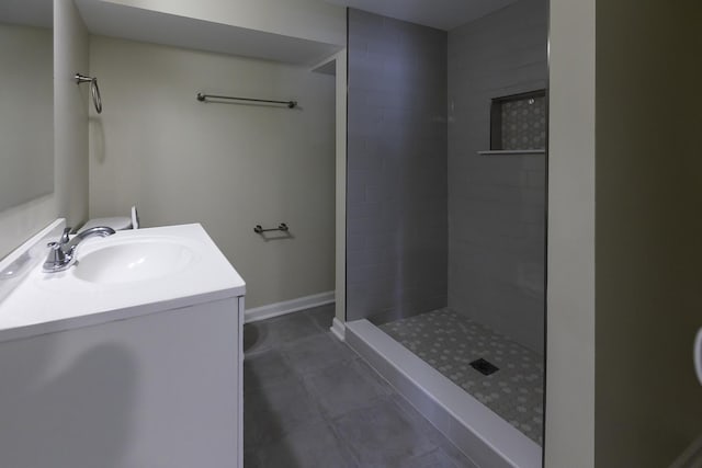 bathroom featuring tile patterned flooring, tiled shower, vanity, and baseboards