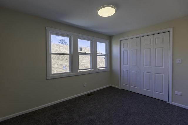 unfurnished bedroom featuring baseboards, visible vents, dark colored carpet, and a closet