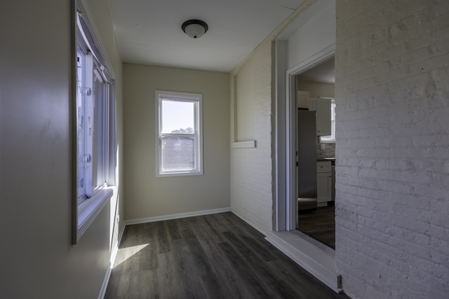 corridor with baseboards, dark wood finished floors, and brick wall